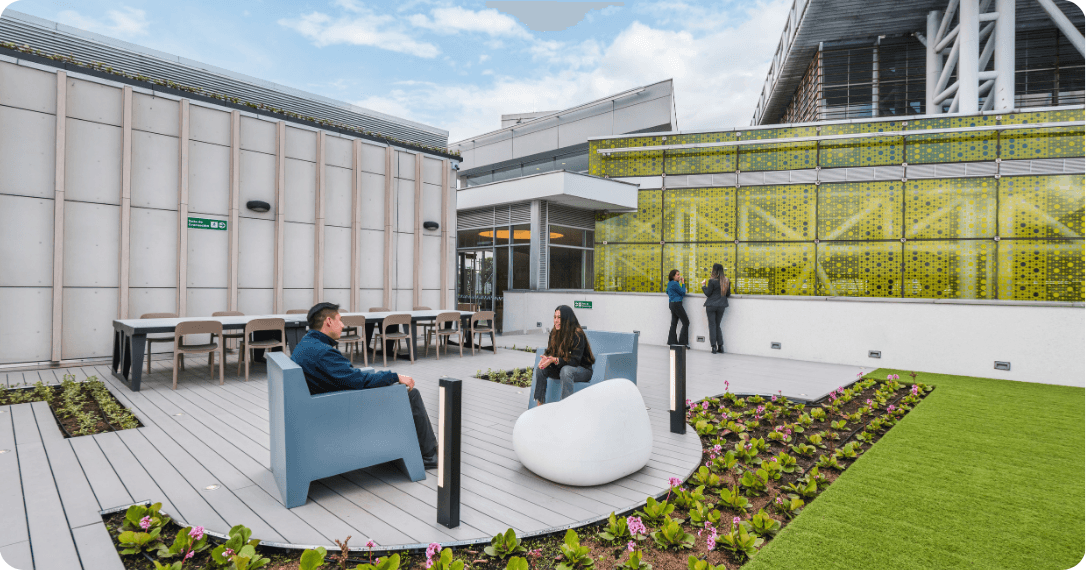 An outdoor terrace coworking area featuring wooden work tables, greenery, and outdoor seating.